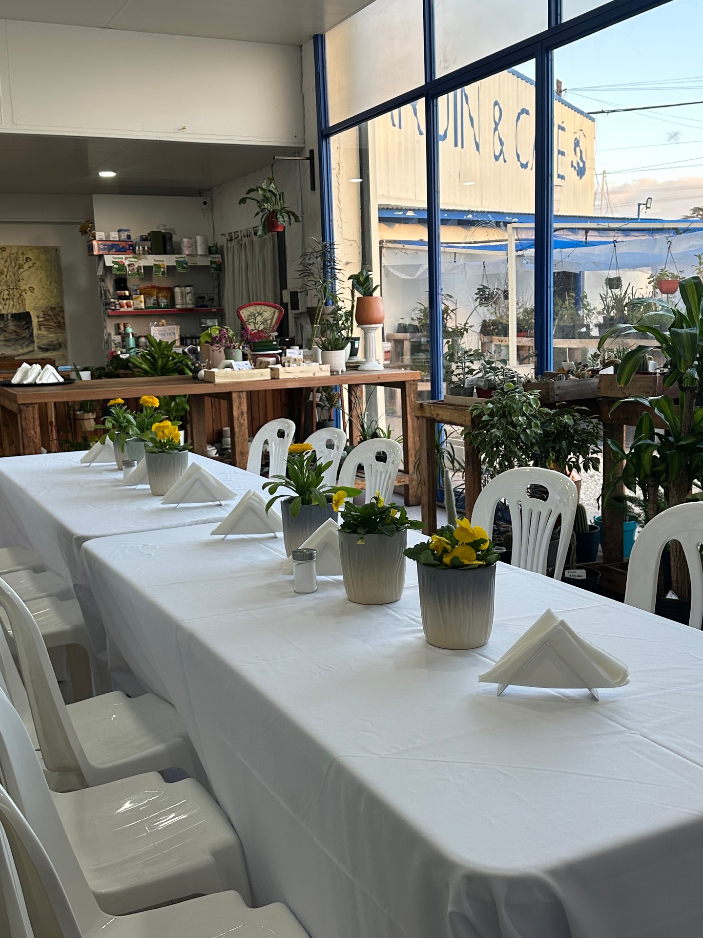 Mesa larga con flores amarillas y luz natural en el vivero-café La Romería